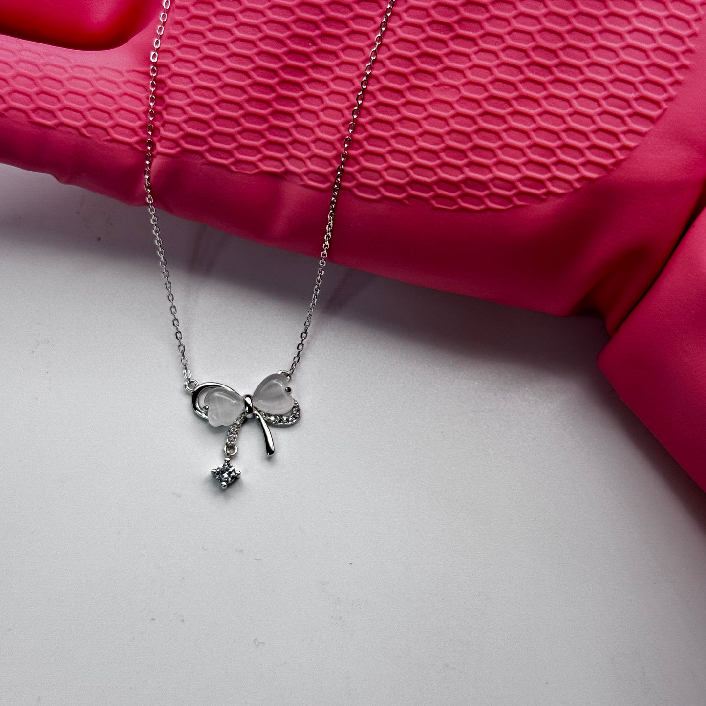 Silver necklace with a pendant on a pink textured surface