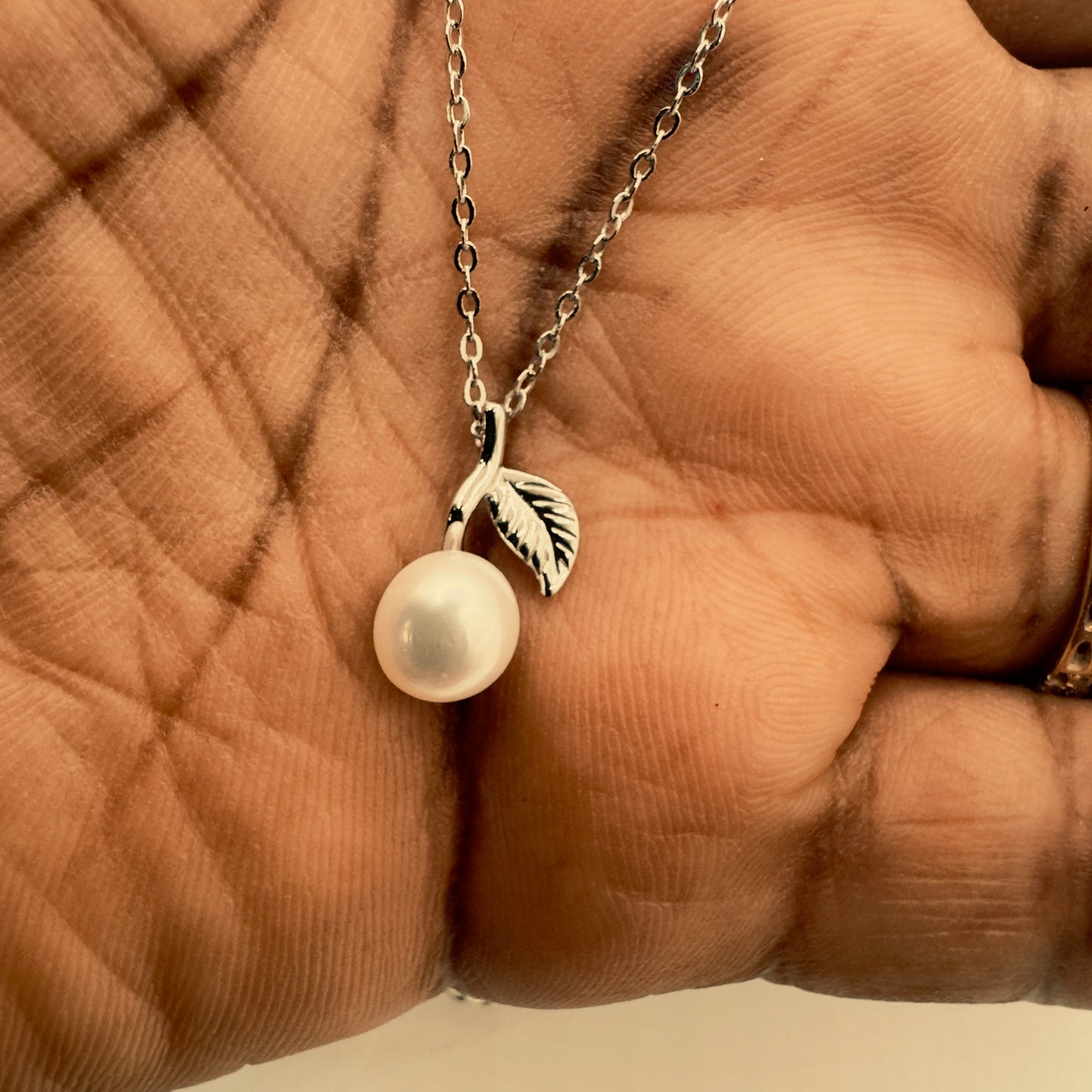 Pearl necklace with leaf pendant held in a hand