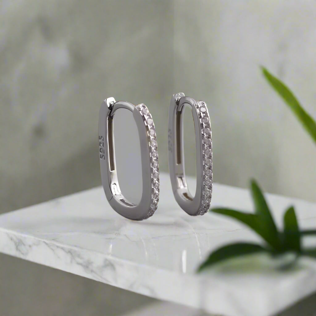 Pair of silver hoop earrings with embedded stones on a gray background