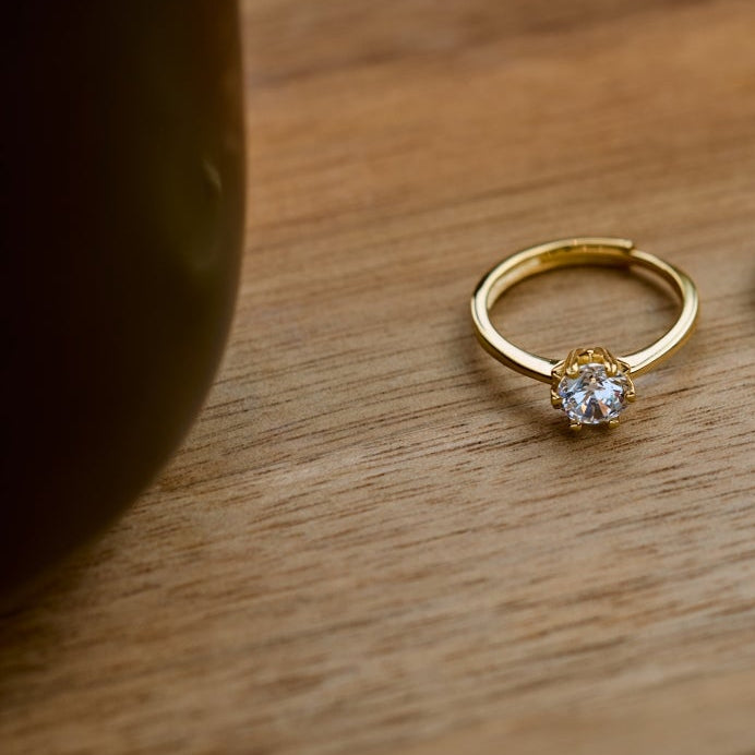 Gold engagement ring on a wooden tray next to a cup of coffee.