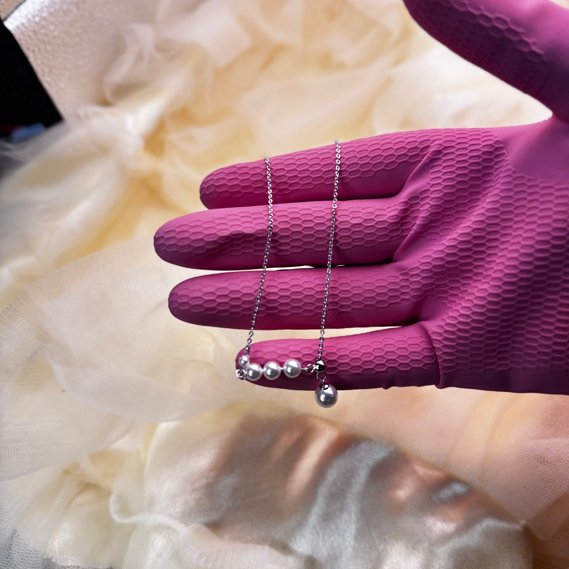 Silver necklace with pearls held by a hand wearing a purple glove against a soft, blurred background.