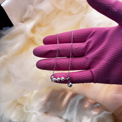 Silver necklace with pearls held by a hand wearing a purple glove against a soft, blurred background.