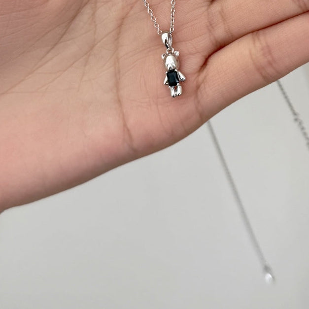 Hand holding a silver necklace, ring, and earrings with black accents on a plain background